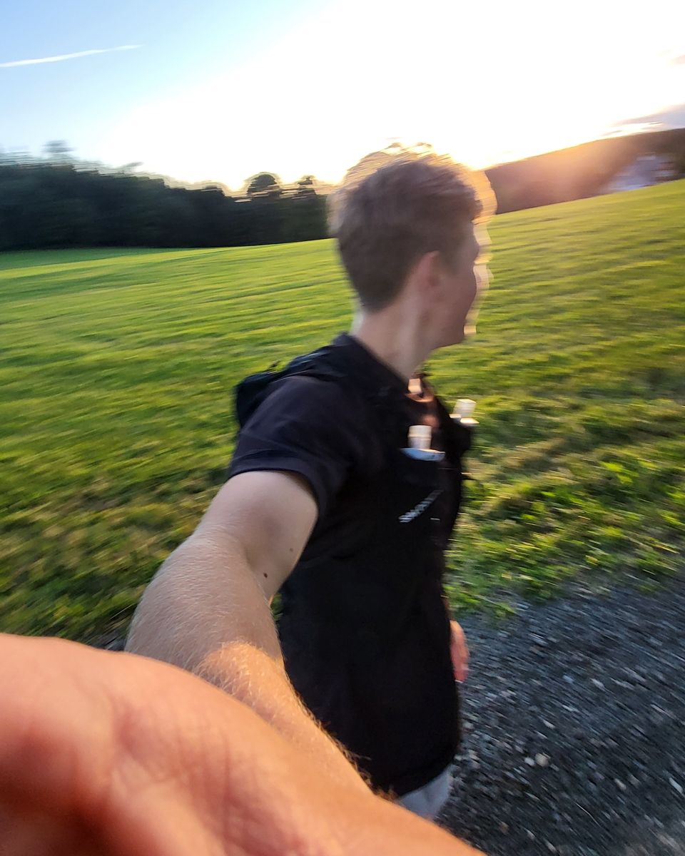 Vítek za běhu s běžeckou vestou, selfie rozmazané pohybem, louka při západu slunce